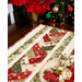 A closer look at the table runner, demonstrating piecing details on the Christmas themed fabrics. A decorated tree and vivid red poinsettias peek into frame from above.