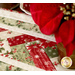 A super close up on the patchwork of the table runner, demonstrating fabric and piecing details; vivid red poinsettias peek into frame from the right side.