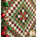 An angled shot of the quilt featuring a patterned design of red, green, and cream, next to a Christmas tree.