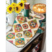 A vintage quilt draped on a countertop next to a vase of yellow flowers and a baked pie