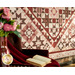 A stylized shot of the bottom of the quilt; in the foreground a chair with a draped coordinating blanket, open book, and pink vase of flowers peek into frame.