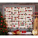 Image of the Hometown Christmas Quilt, a christmas quilt in white, green, red, and black, with pieced presents, words, houses, and trees. The quilt is hung on a wall with Christmas decorations surrounding it 