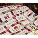 Photo of a christmas quilt in white, green, red, and black, with pieced presents, words, houses, and trees