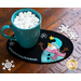 A teal cup filled with marshmallows rests on a black felt coaster featuring a snowman design and snowflakes scattered around.