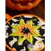 A cloth hot pad made with ghost fabric and an orange border on a wood table with Halloween decor
