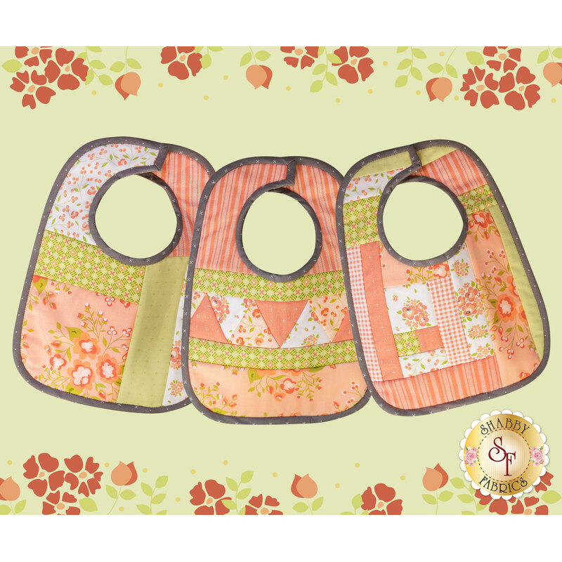 The three Baby Bibs made with Apricot & Ash fabrics on a green background