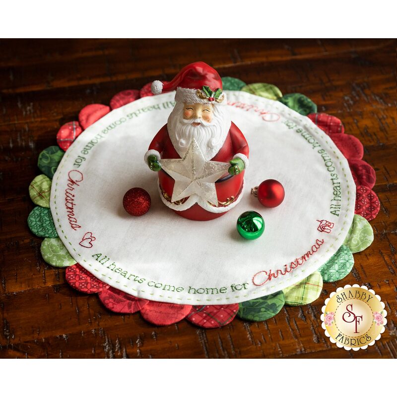 Round scalloped Christmas themed table topper with a Santa Claus figure and ornaments on top