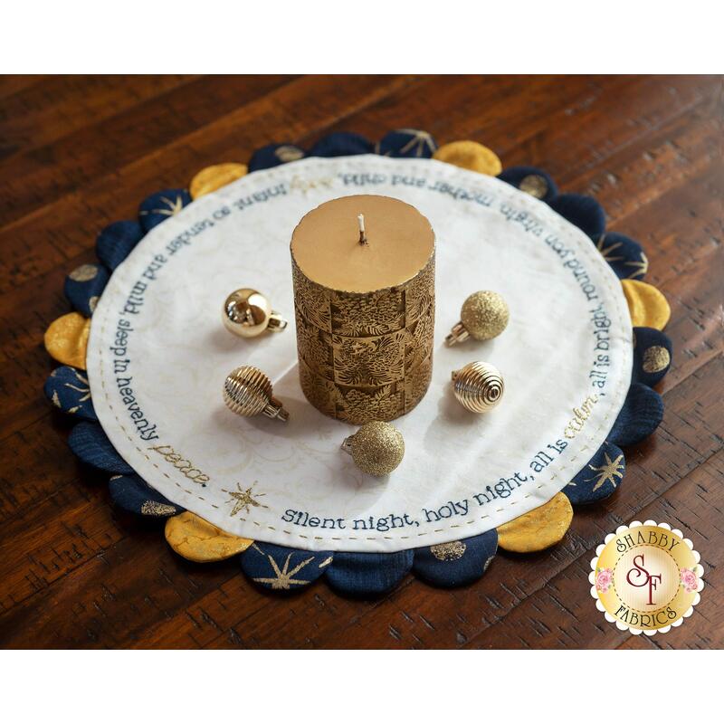 A gold candle and ornaments displayed on top of the Silent Night Scalloped Table Topper