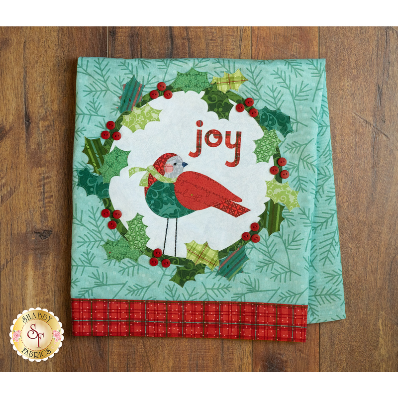 Tea towel with a laser cut applique bird and wreath hung from clothes pins