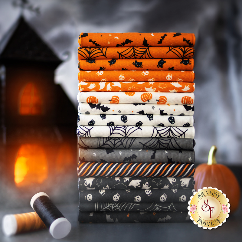 A stack of Halloween fabrics in orange, white, gray, and black included in the Holiday Essentials Halloween FQ Set.