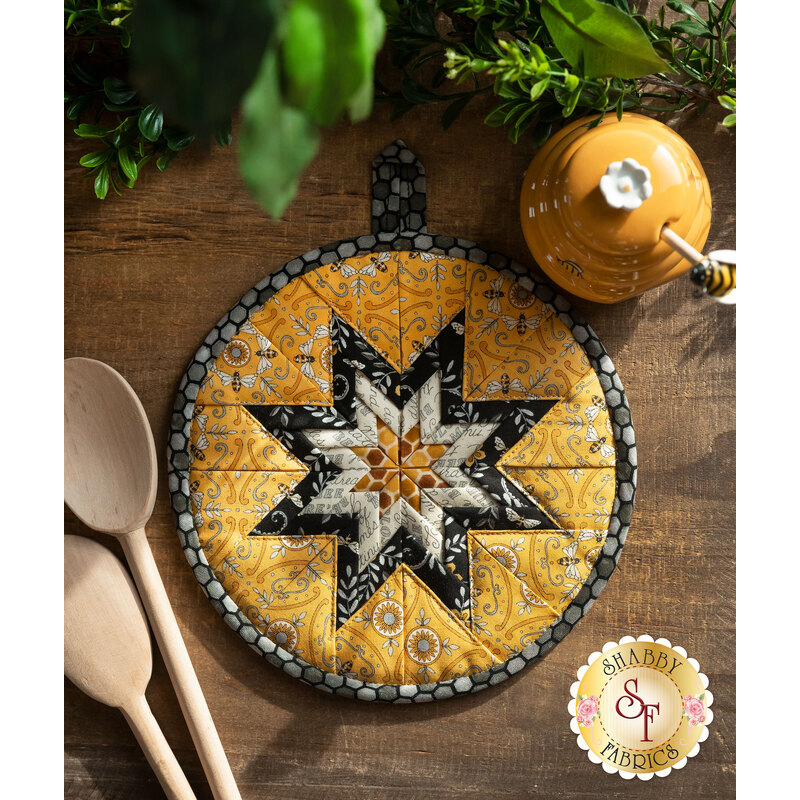 Yellow, black, and cream Folded Star Hot Pad laid flat on a wood table