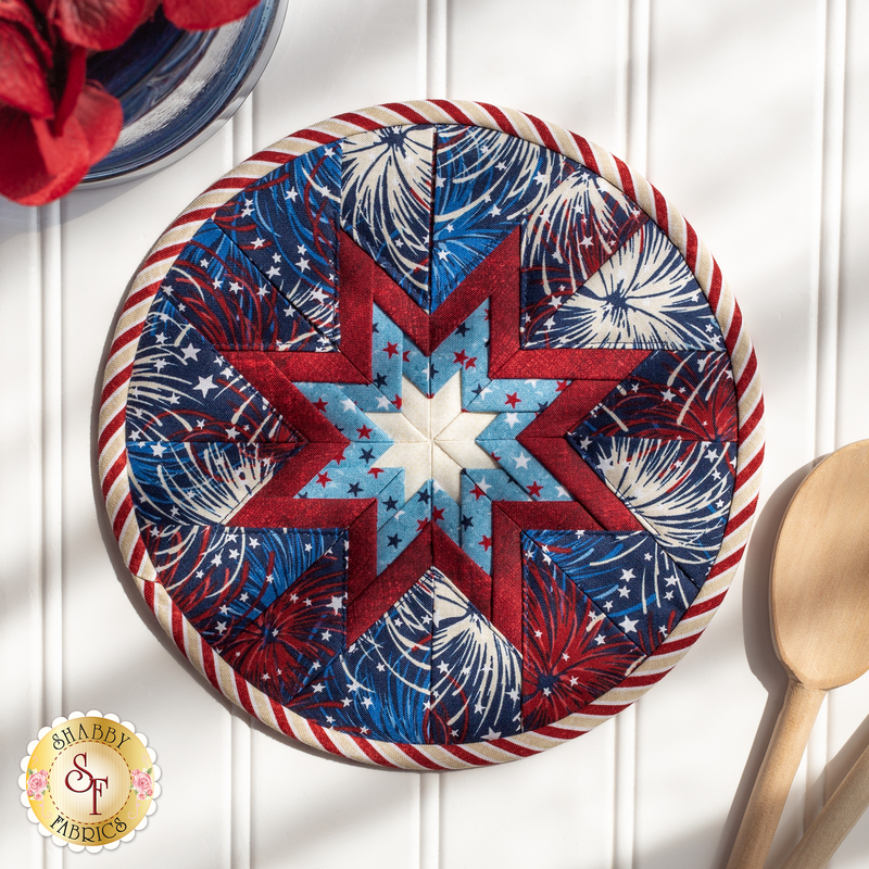 Patriotic themed hot pad with fireworks laid flat on a wood table