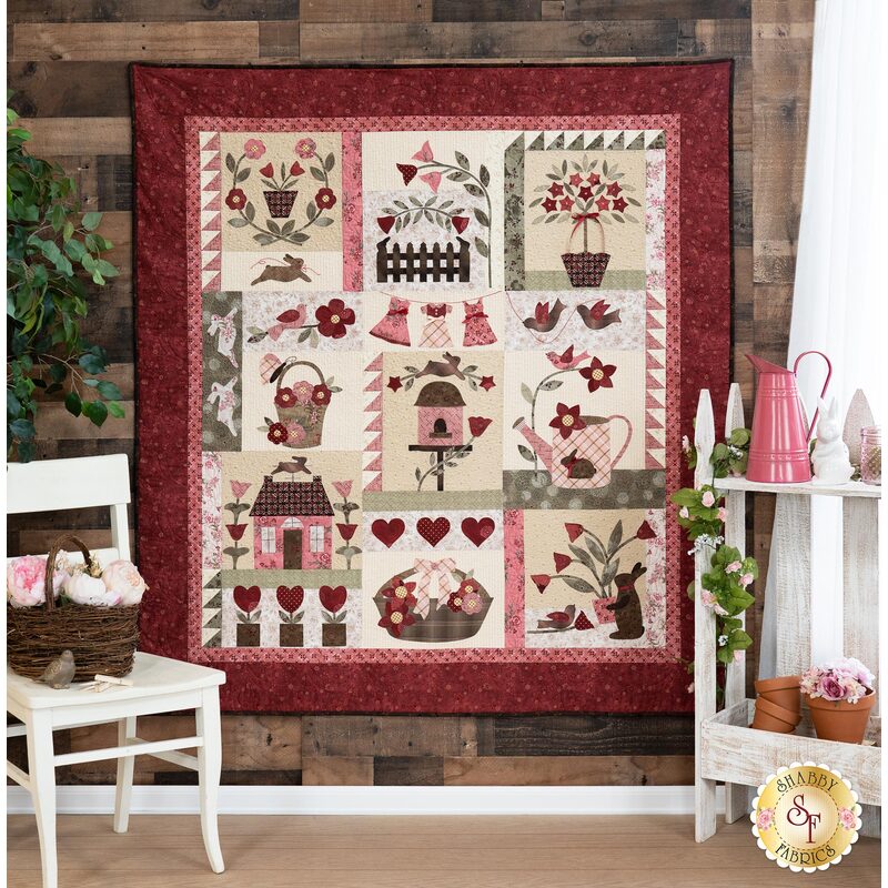 The beautiful Le Jardin quilt hanging from a wood plank wall