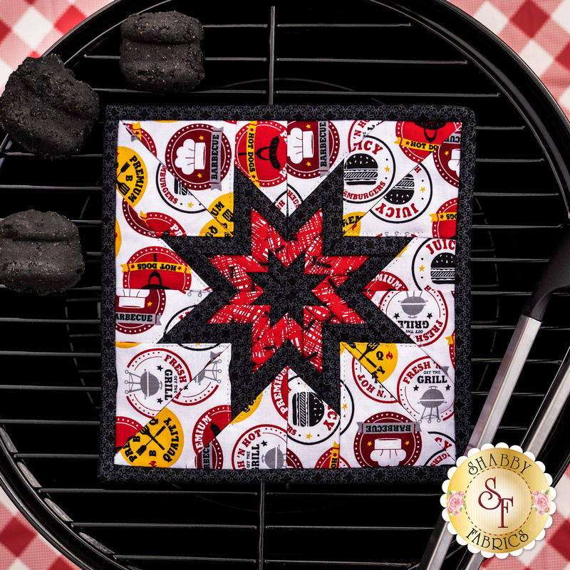The red and white Peace, Love & BBQ Folded Star Squared Hot Pad laid flat on a BBQ grill