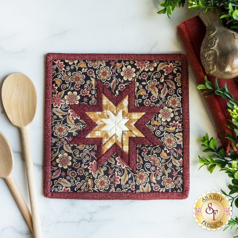 A quilted hot pad with a folded star in the middle and floral background on a white marble countertop
