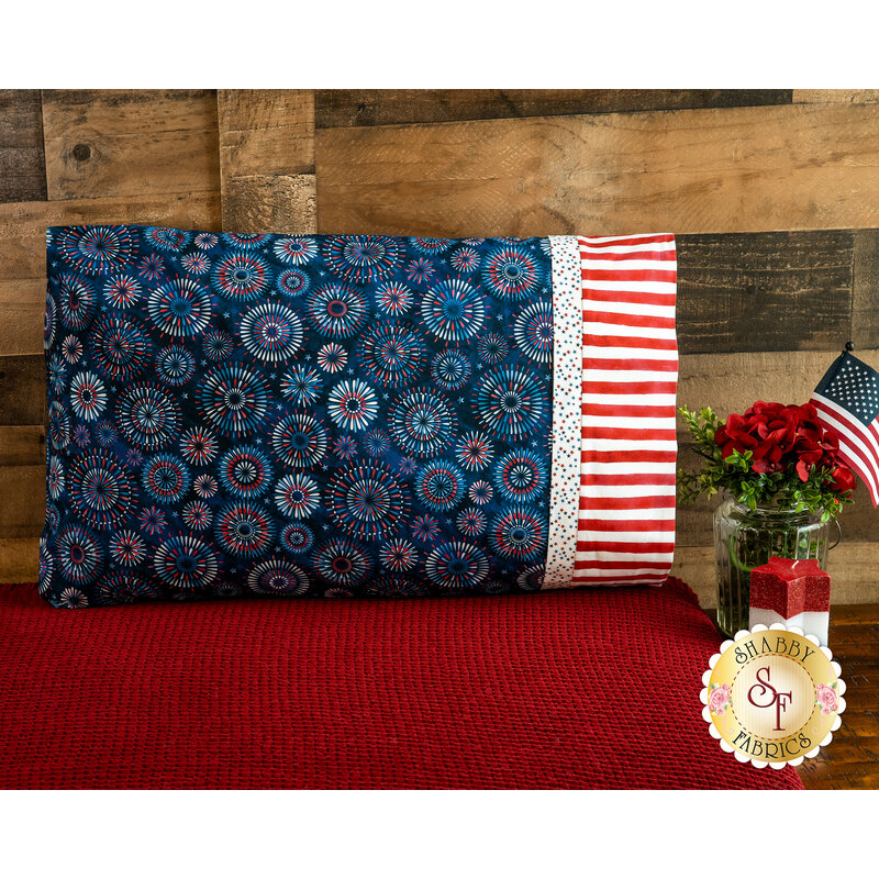 A patriotic pillowcase featuring bursting fireworks propped up against a wood wall 