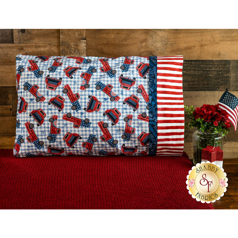 A patriotic pillowcase featuring classic gingham and vintage trucks propped up against a wood wall 