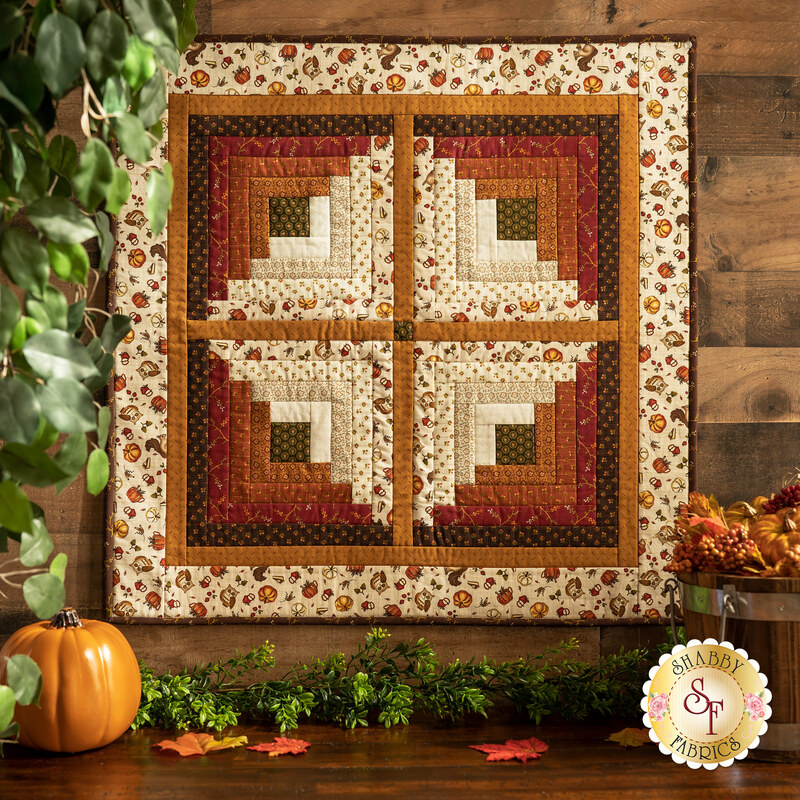 Earth tone colored quilt with autumn motifs hanging from a wall.