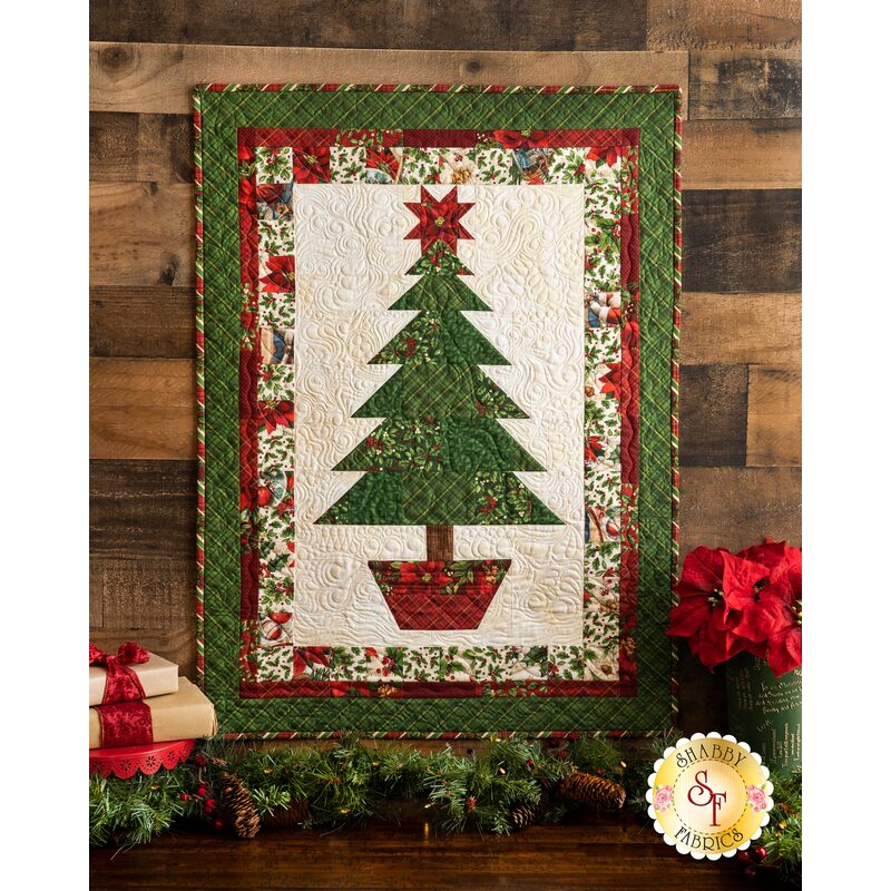 Christmas themed quilt with green and red border around large central Christmas tree on cream background.