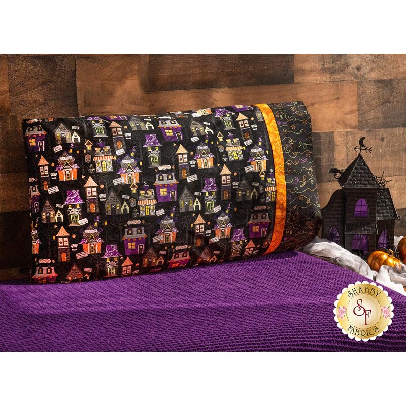 Black halloween themed pillowcase featuring haunted houses on a purple blanketed bed.