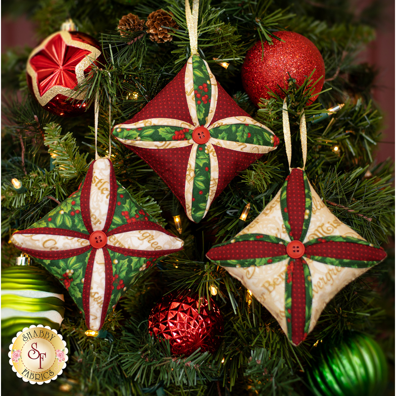 Three Christmas tree ornaments, sewn with holiday themed fabrics, hanging from a decorated Christmas tree.