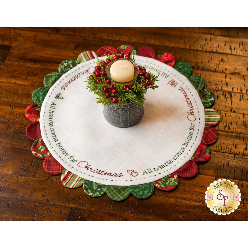 Christmas themed embroidered table topper on wood table with candle.