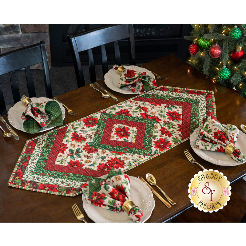 Christmas themed floral table topper on wood table next to matching cloth napkins. 