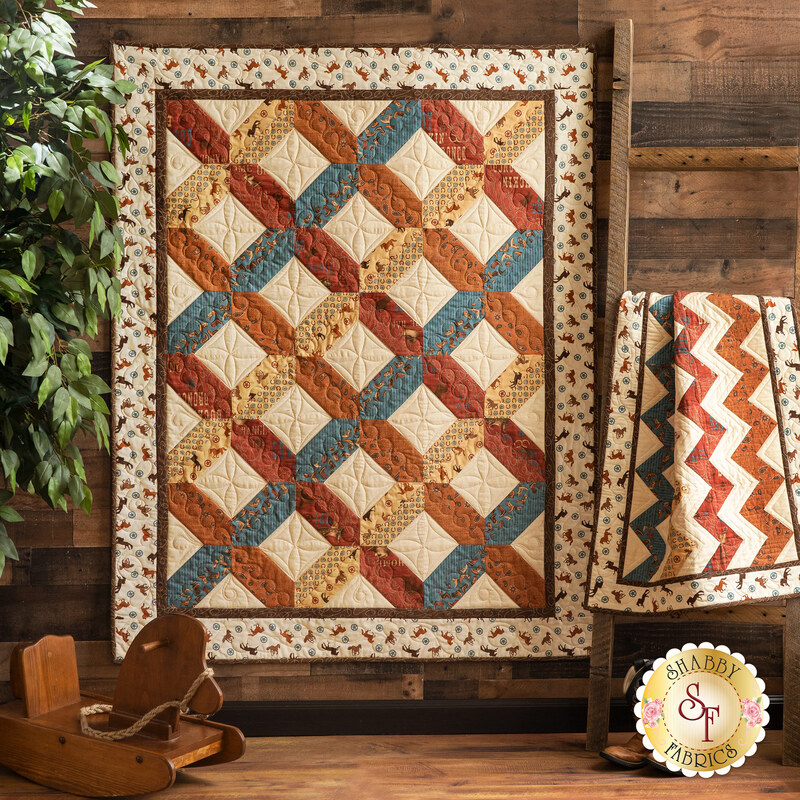 One large earth toned, cowboy themed quilt hanging next to a matching, smaller quilt that is draped over furniture.