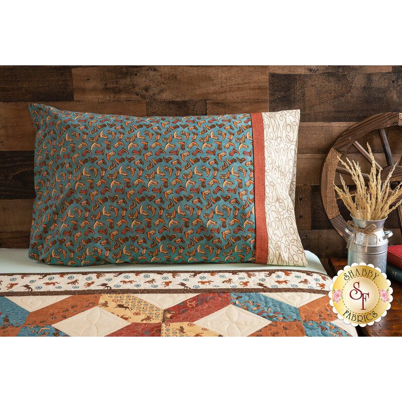 Teal colored pillowcase featuring cowboy boots resting on bed with matching cowboy themed quilt.