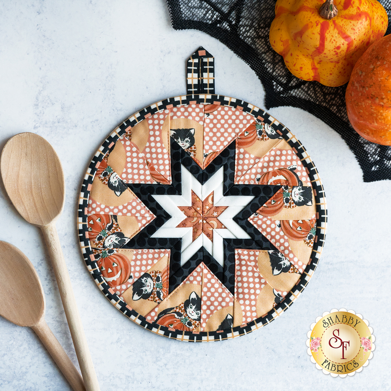 Round hot pad with central folded star, featuring white on peach polkadots and cartoon cats with jack-o-lanterns.