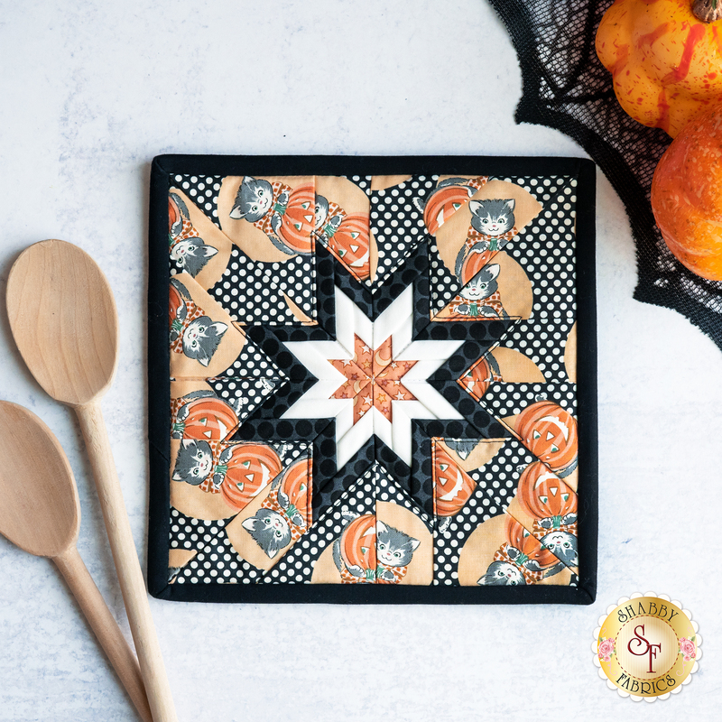 Square hot pad with central folded star, featuring white on black polka dots with cartoon cats and jack-o-lanterns.
