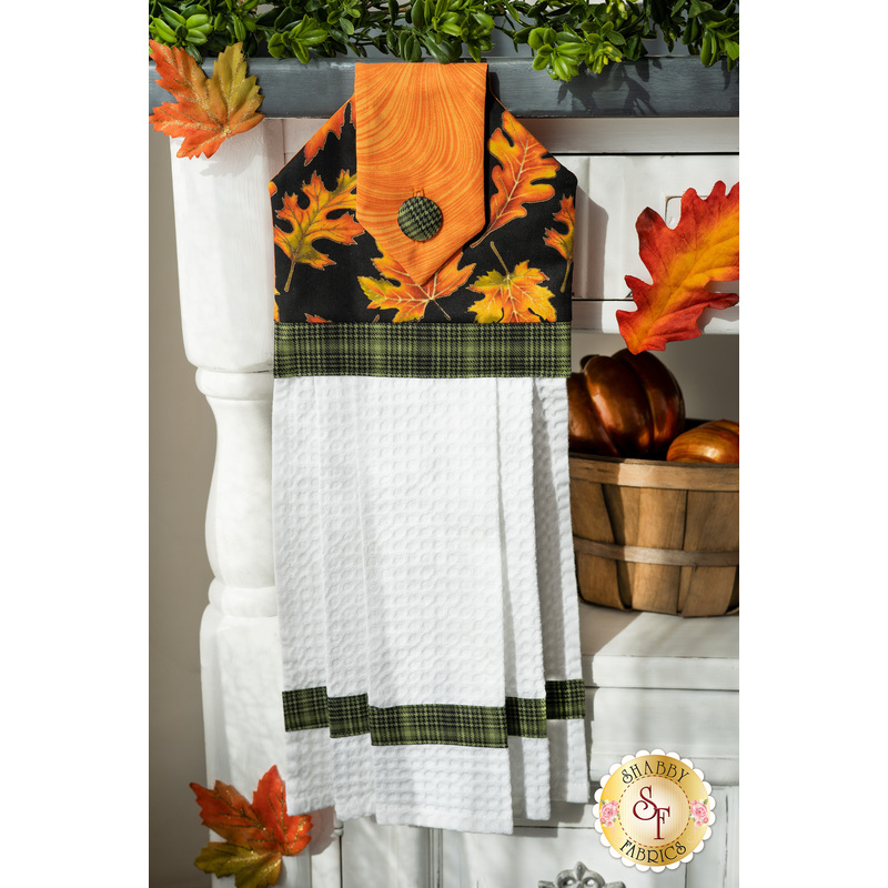 Autumn themed towel featuring leaves on a dark background with orange, and green gingham accents.
