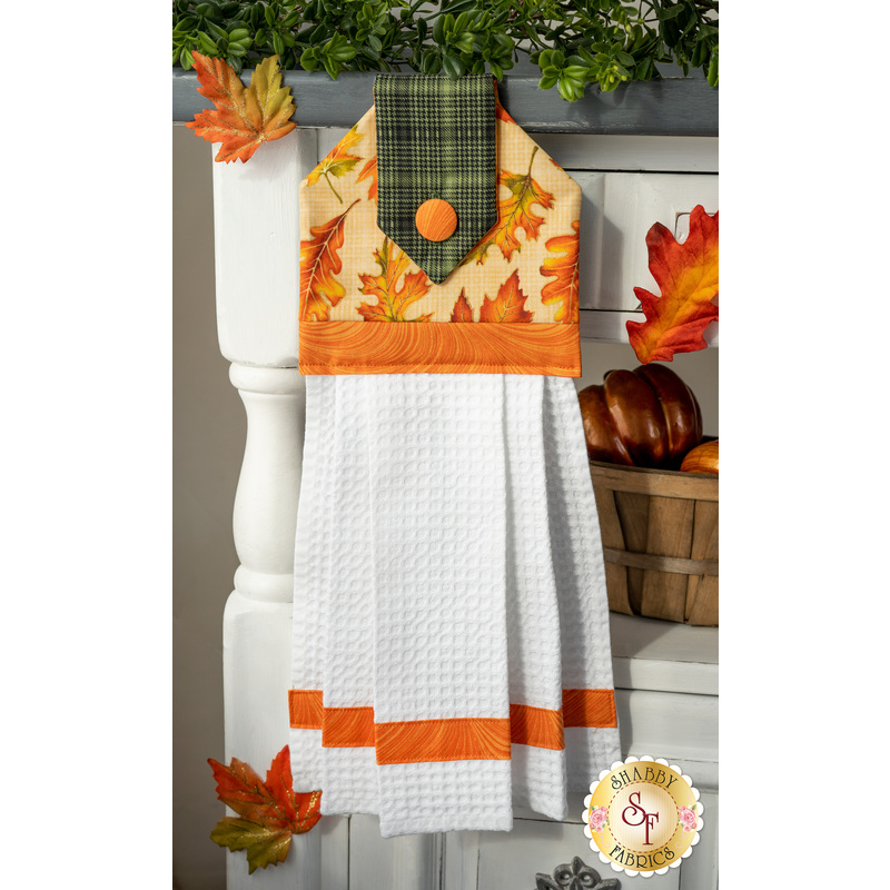 Autumn themed towel featuring leaves on a cream background with orange, and green gingham accents.