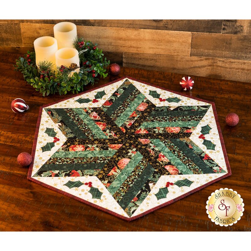 Diamond design table topper featuring strips of green Christmas themed fabrics and laser-cut holly appliqué on cream.