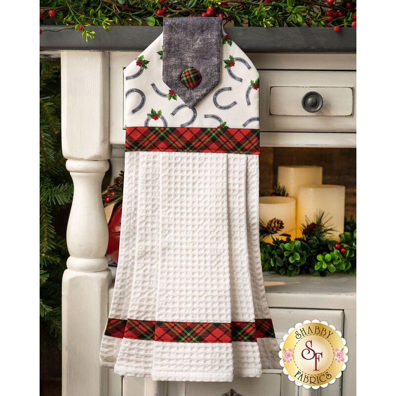 Christmas themed towel with horseshoes and holly tossed on white with red and green gingham button and banding.