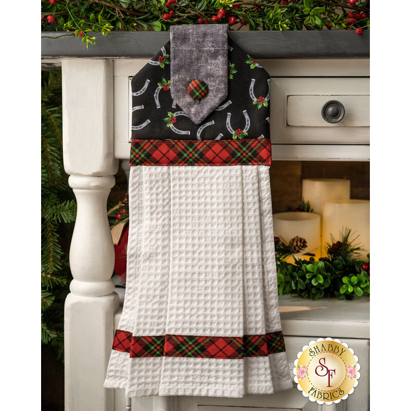 Christmas themed towel with horseshoes and holly tossed on black with red and green gingham button and banding.