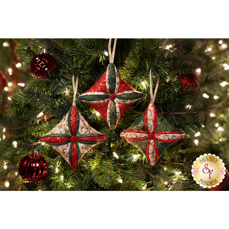 Three Christmas tree ornaments, sewn with holiday themed fabrics, hanging from a decorated Christmas tree.