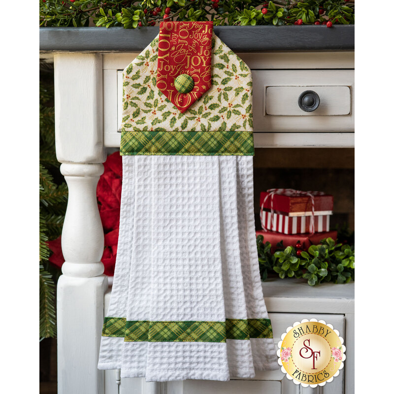 Cream hanging towel featuring metallic holly print with green gingham and red with gold wording accents.