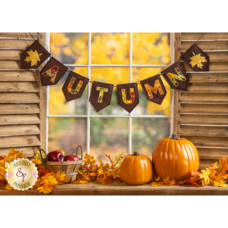 Banner of pennants spelling out the word autumn hanging over pumpkins in front of a window.