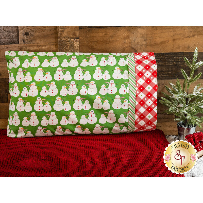 Pillowcase featuring snowmen on green with red on white gingham at the opening edge.