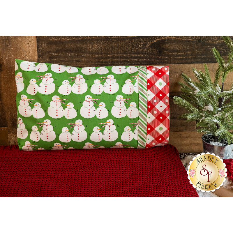 Pillowcase featuring snowmen on green with red on white gingham at the opening edge.