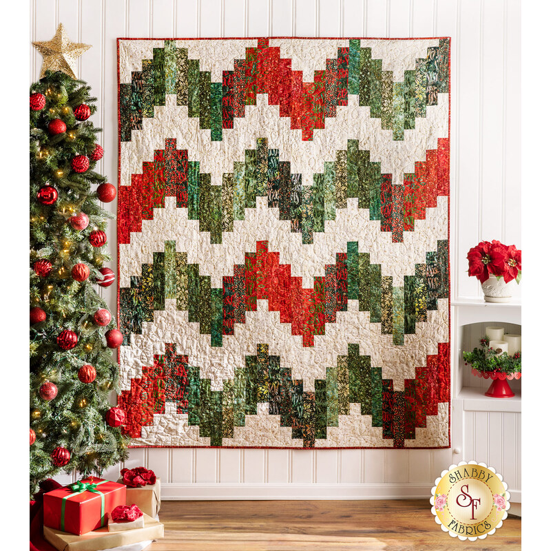 Quilt made of green and red holiday themed fabrics in a zig zag stripe design on cream, hanging from a white wall.