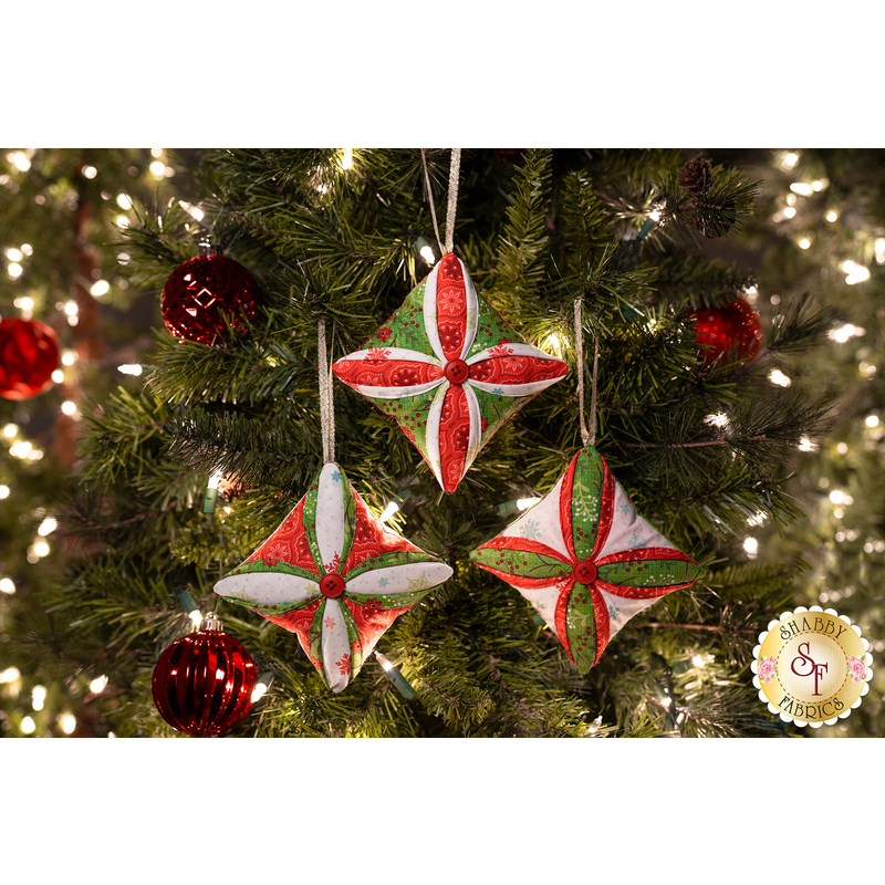 Three Christmas tree ornaments, sewn with holiday themed fabrics, hanging from a decorated Christmas tree.