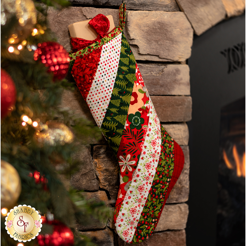 Hanging holiday stocking made from strips of Christmas themed fabric in red, green, and white.