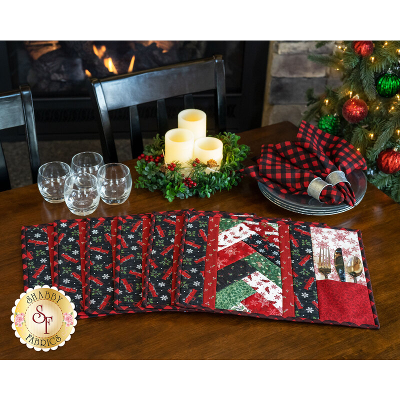 Six holiday placemats made of red, green, black, and white fabrics arranged on wood table.
