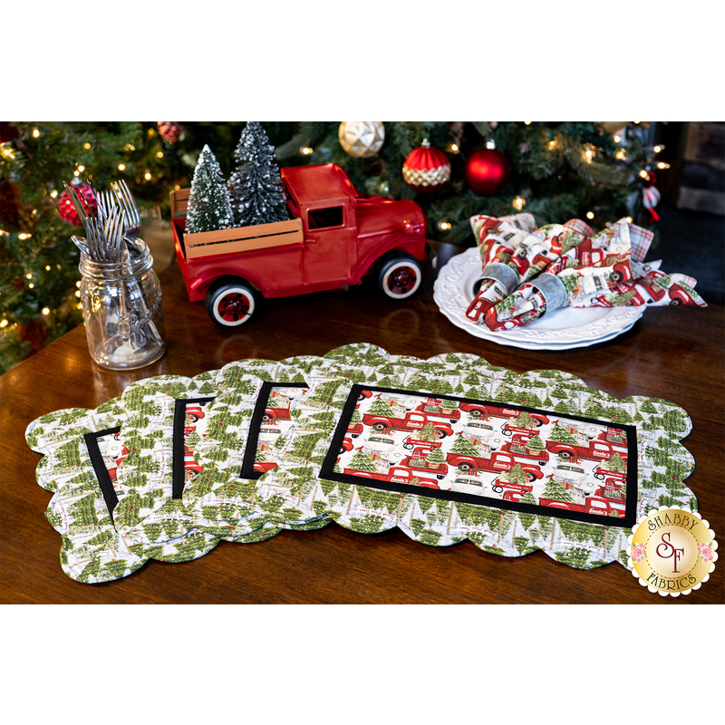 Christmas themed scalloped placemats featuring red trucks, wagons, and pine trees.