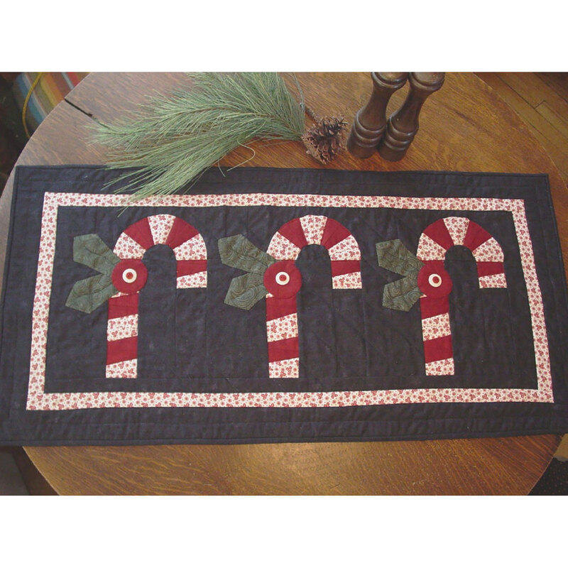 The finished Twisted Peppermint table runner laid flat on a wood table with salt and pepper shakers and a pine sprig.