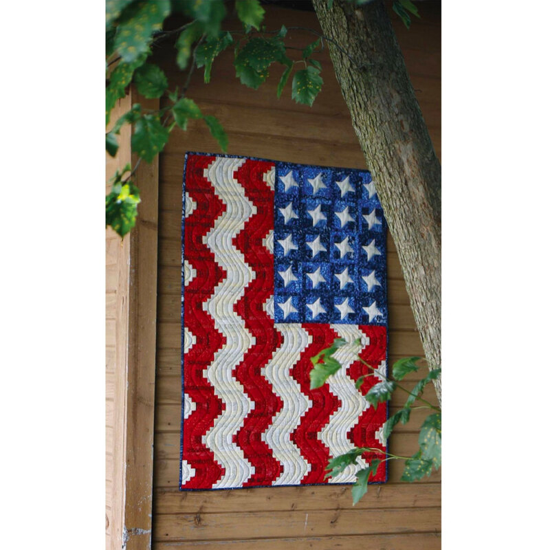 The finished America the Beautiful quilt draped on a wood wall