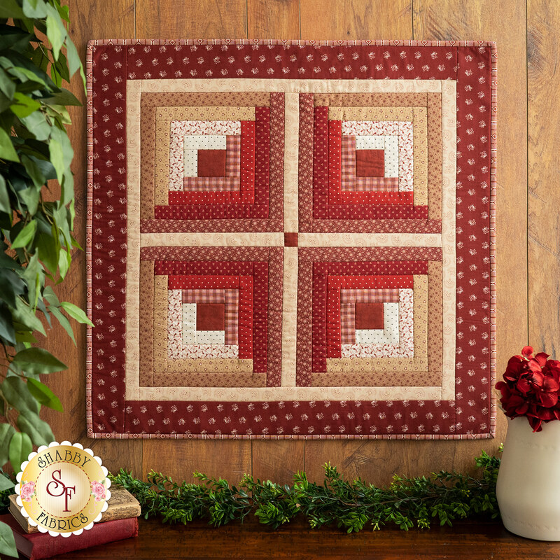 Wall hanging with four squares made up of strips of red and cream floral and geometric fabric prints.