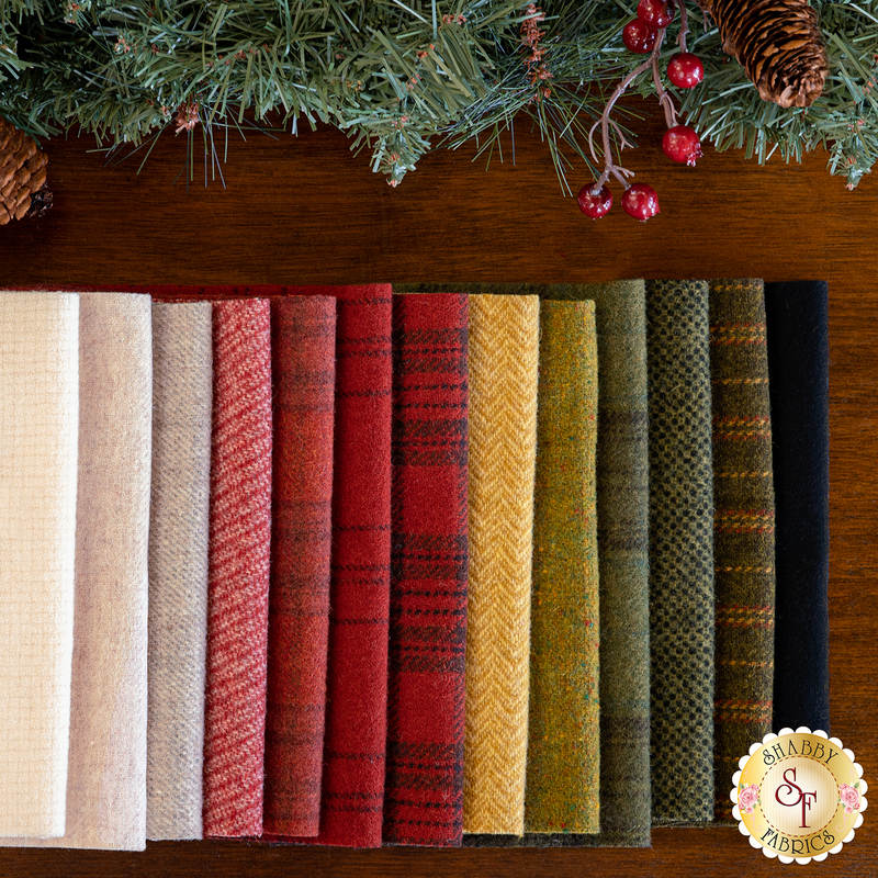 13 pieces of wool laid flat on a wood table next to pine sprigs and berries
